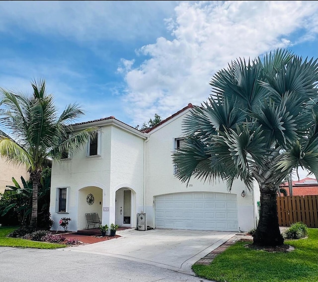 mediterranean / spanish-style house with stucco siding, driveway, an attached garage, and fence