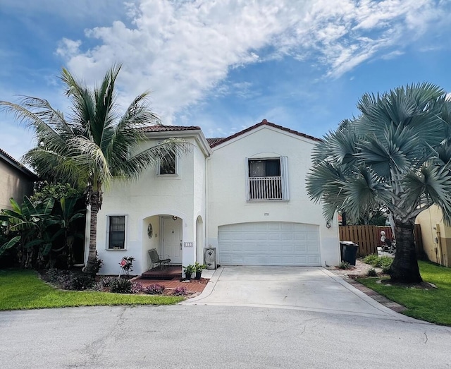 mediterranean / spanish-style house with stucco siding, fence, a tile roof, an attached garage, and driveway