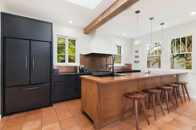 kitchen with custom range hood, backsplash, paneled built in fridge, a skylight, and butcher block counters