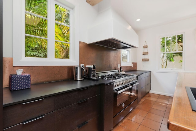 kitchen featuring modern cabinets, custom range hood, dark countertops, light tile patterned floors, and gas range