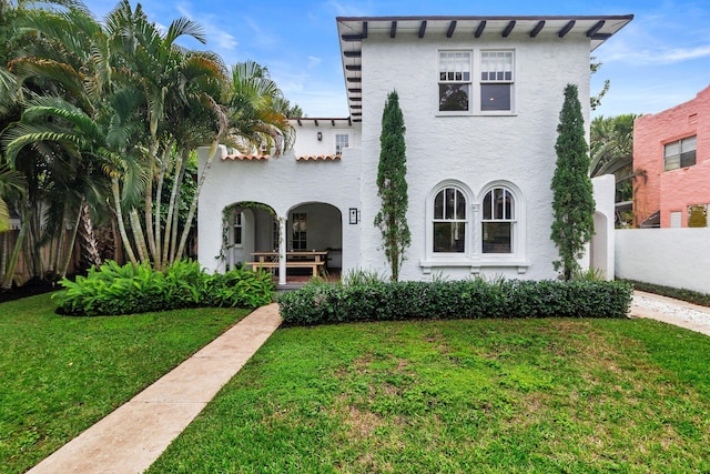 mediterranean / spanish-style house with stucco siding, a front lawn, and fence