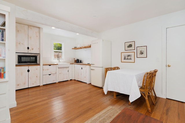 kitchen featuring open shelves, freestanding refrigerator, a sink, stainless steel microwave, and light wood-type flooring