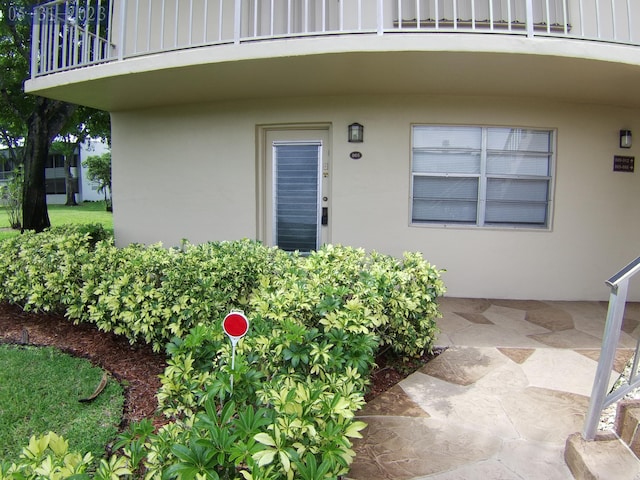 property entrance with stucco siding, a balcony, and board and batten siding