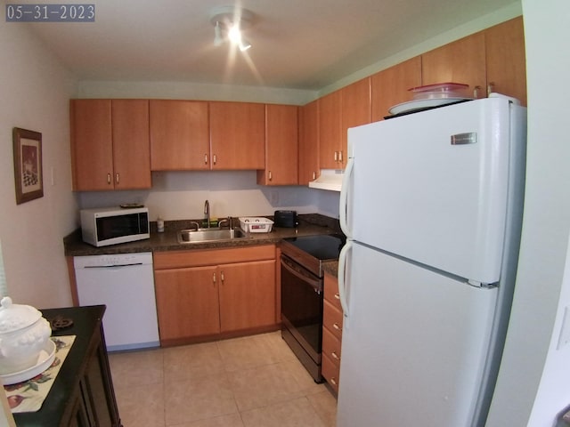 kitchen featuring a sink, under cabinet range hood, dark countertops, white appliances, and light tile patterned floors