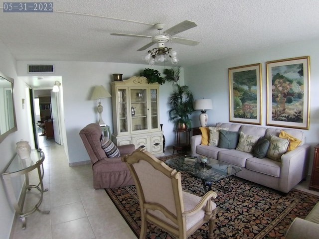 living area featuring light tile patterned floors, visible vents, a textured ceiling, and a ceiling fan