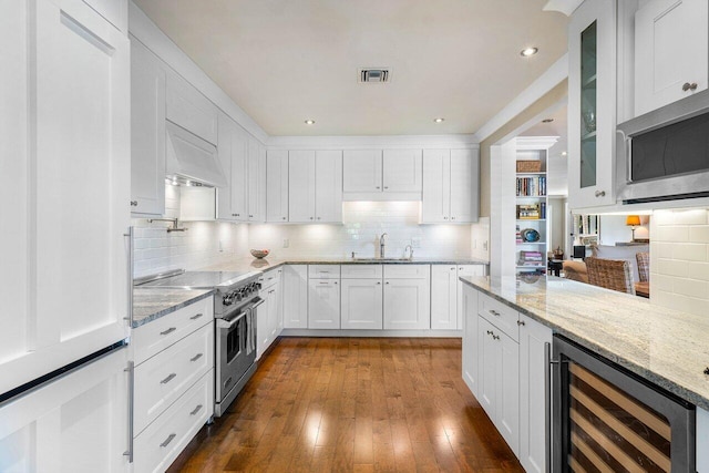 kitchen featuring beverage cooler, custom range hood, a sink, appliances with stainless steel finishes, and glass insert cabinets