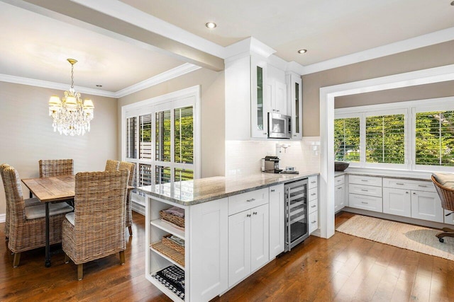 kitchen featuring beverage cooler, stainless steel microwave, white cabinetry, and light stone countertops