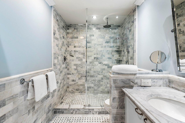 bathroom featuring vanity, a wainscoted wall, a stall shower, tile walls, and toilet