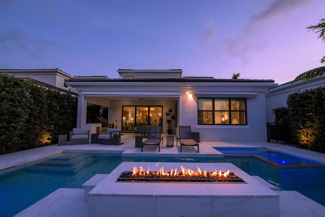 back of house with a patio, an in ground hot tub, an outdoor pool, stucco siding, and an outdoor living space with a fire pit