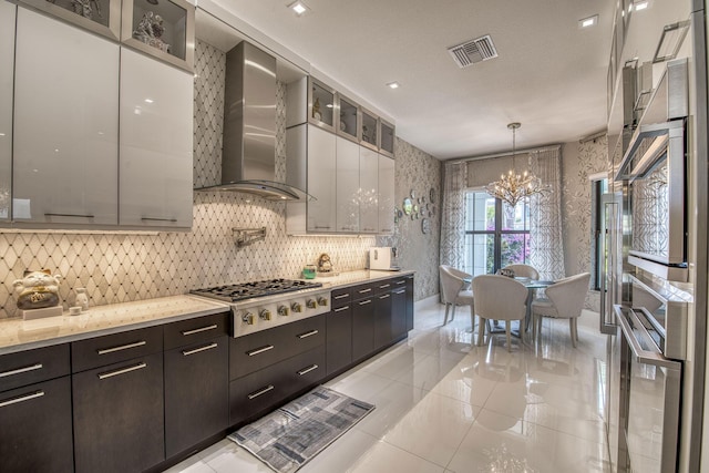 kitchen featuring visible vents, wallpapered walls, glass insert cabinets, stainless steel gas cooktop, and wall chimney exhaust hood