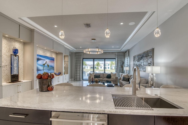 kitchen featuring visible vents, a raised ceiling, open floor plan, and a sink