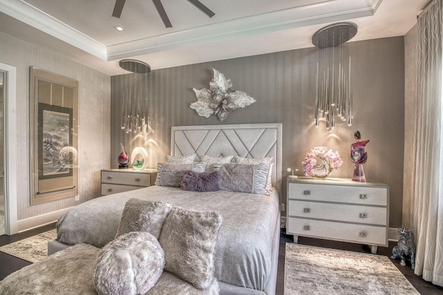 bedroom featuring wood finished floors, a ceiling fan, baseboards, a tray ceiling, and ornamental molding