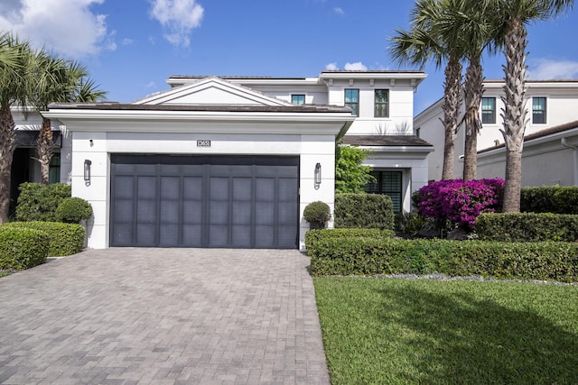 view of front of property featuring an attached garage, stucco siding, a front lawn, a tiled roof, and decorative driveway