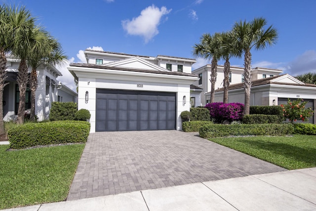 view of front facade featuring stucco siding, an attached garage, decorative driveway, and a front yard