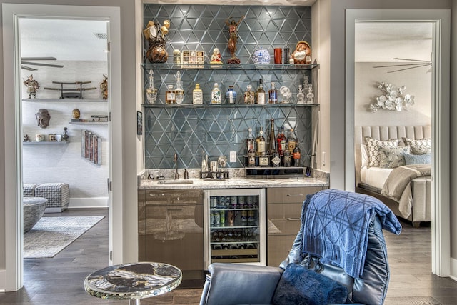 bar featuring beverage cooler, a sink, backsplash, wood finished floors, and indoor wet bar