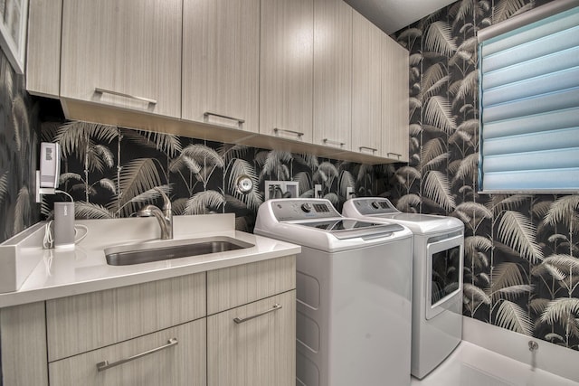 washroom with a sink, wallpapered walls, cabinet space, and washer and dryer