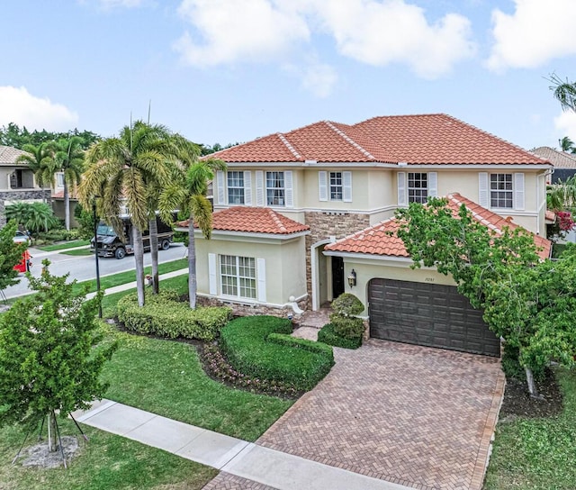 mediterranean / spanish-style house with stucco siding, decorative driveway, stone siding, a garage, and a tiled roof