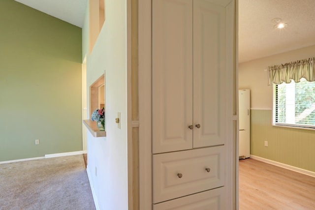 hallway with light wood-type flooring, baseboards, wood walls, and wainscoting