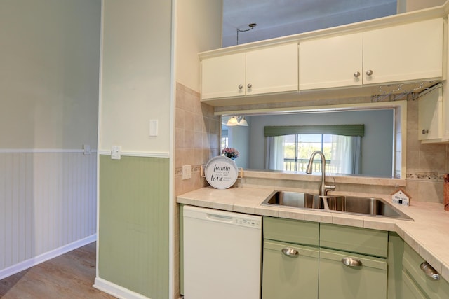 kitchen featuring light wood-style flooring, white dishwasher, a sink, wainscoting, and green cabinets