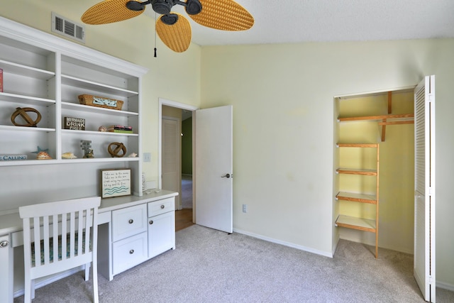 office space with a ceiling fan, visible vents, baseboards, built in desk, and light colored carpet