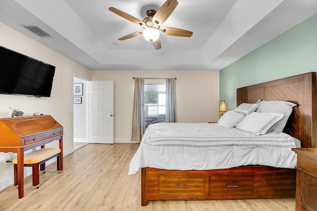 bedroom with a ceiling fan, wood finished floors, visible vents, baseboards, and a tray ceiling