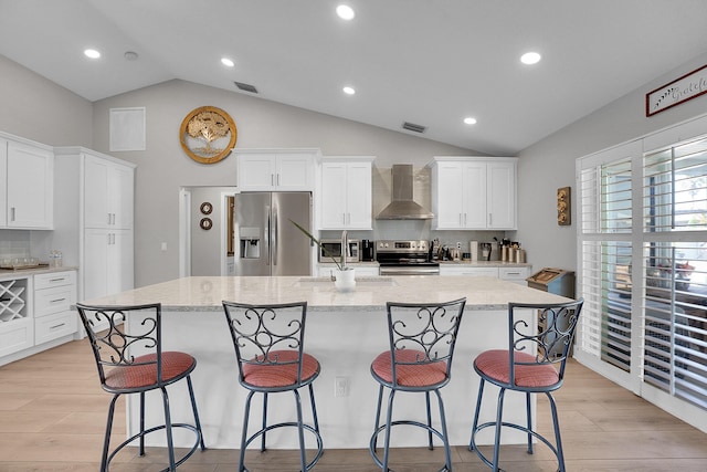 kitchen featuring visible vents, light wood-style flooring, a large island with sink, stainless steel appliances, and wall chimney exhaust hood