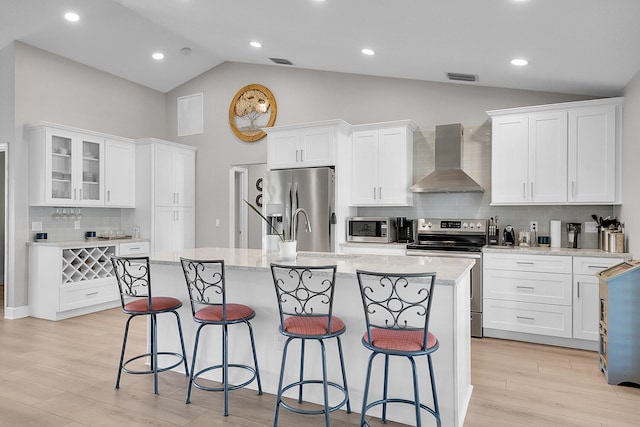 kitchen featuring visible vents, a breakfast bar, stainless steel appliances, white cabinets, and wall chimney exhaust hood