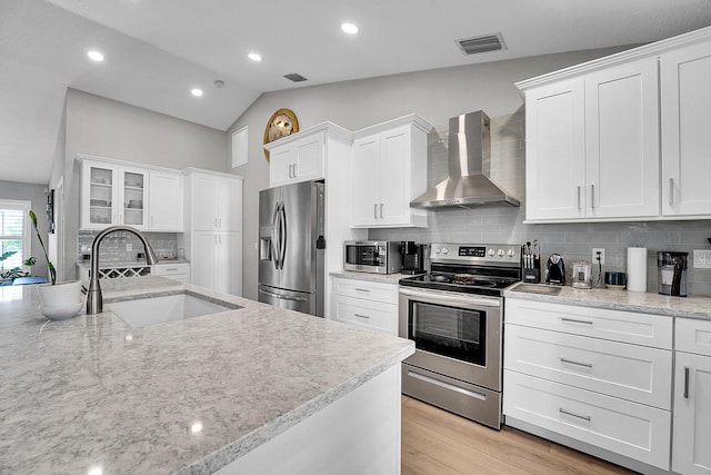 kitchen featuring visible vents, a sink, stainless steel appliances, white cabinets, and wall chimney exhaust hood