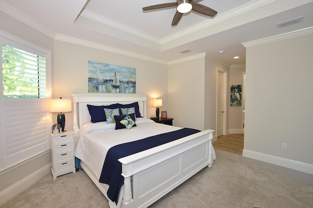 bedroom with a tray ceiling, ornamental molding, visible vents, and light carpet