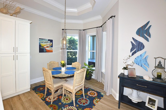 dining room featuring crown molding, a raised ceiling, light wood-type flooring, and baseboards