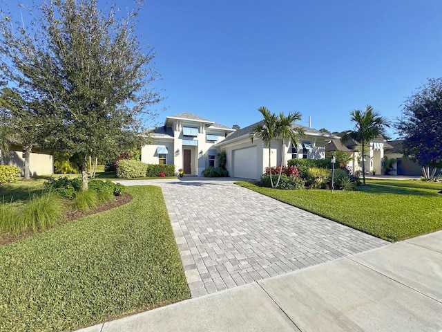 prairie-style home featuring a front lawn, decorative driveway, an attached garage, and stucco siding