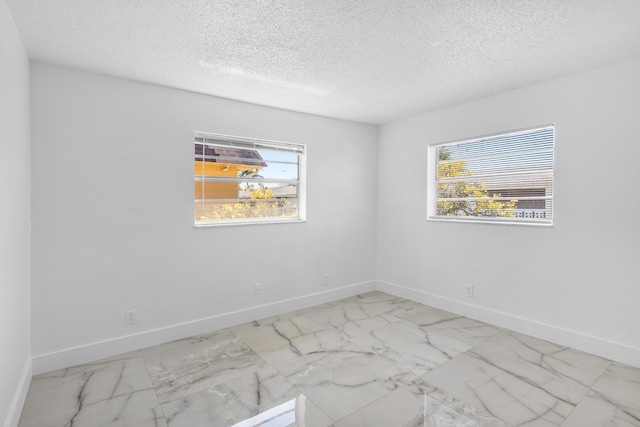 spare room featuring plenty of natural light, marble finish floor, and baseboards