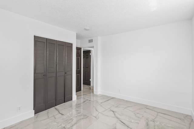 unfurnished bedroom with baseboards, marble finish floor, and a textured ceiling