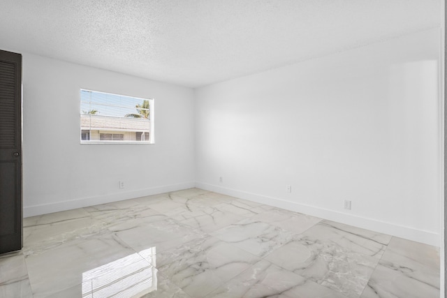 empty room with baseboards, marble finish floor, and a textured ceiling