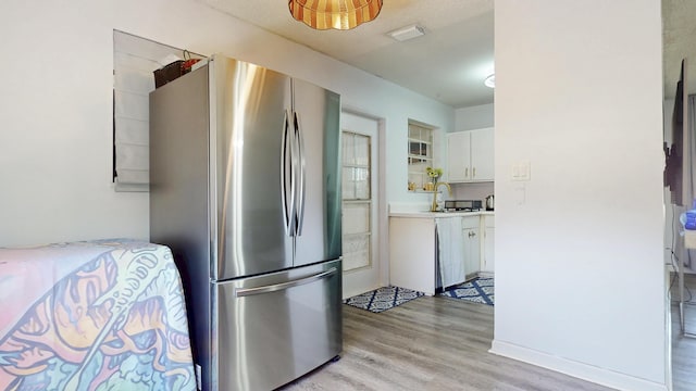 kitchen with light countertops, light wood-style flooring, freestanding refrigerator, white cabinetry, and a sink