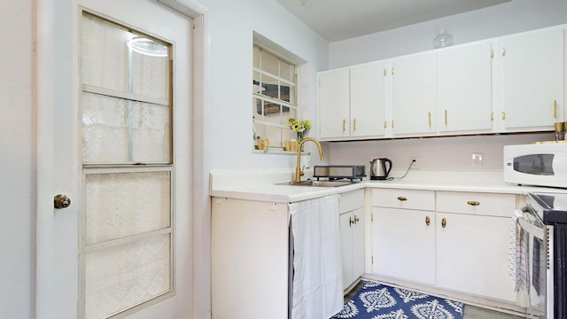 kitchen with stainless steel range with electric stovetop, a sink, white cabinets, light countertops, and white microwave