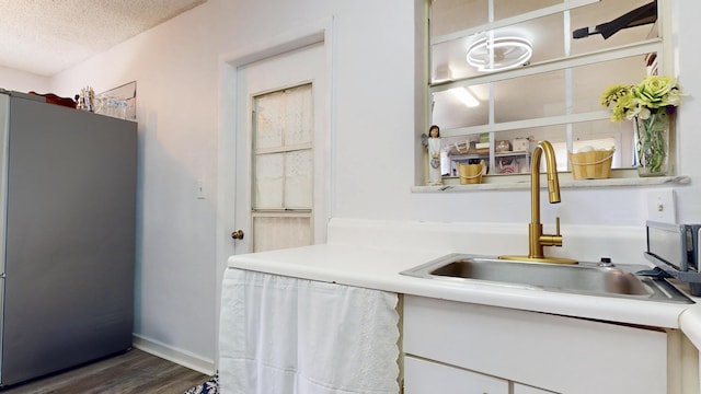 kitchen with dark wood finished floors, freestanding refrigerator, a sink, light countertops, and a textured ceiling