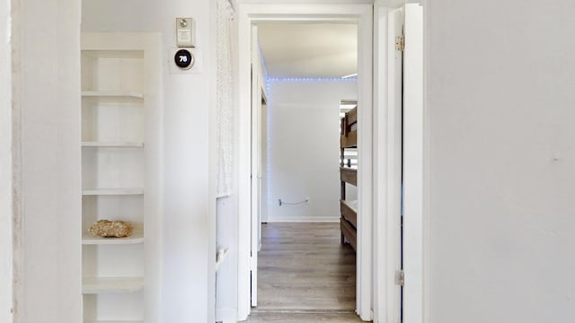 corridor with built in features, wood finished floors, and baseboards