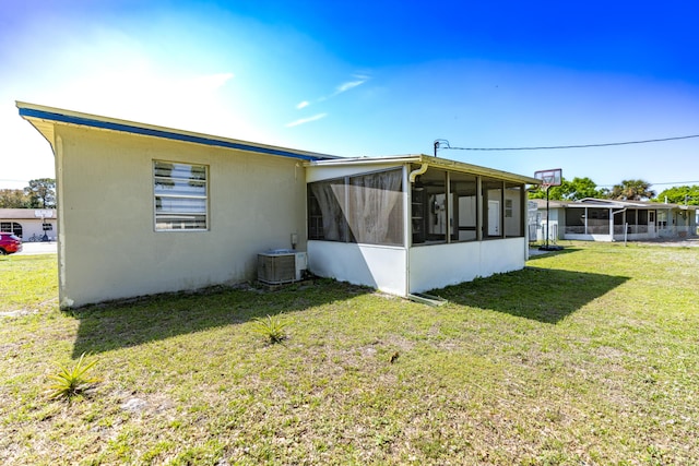 rear view of house with central air condition unit, a lawn, and a sunroom