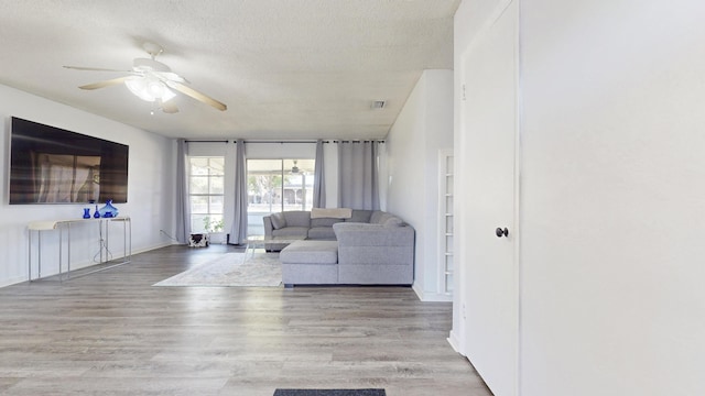 unfurnished living room with a ceiling fan, visible vents, wood finished floors, baseboards, and a textured ceiling