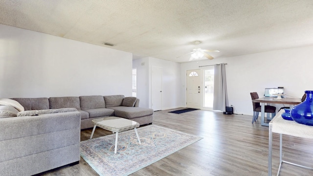 living room featuring a ceiling fan, wood finished floors, visible vents, and a textured ceiling