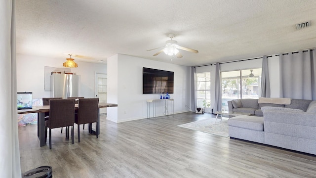 living area featuring ceiling fan, wood finished floors, visible vents, and a textured ceiling