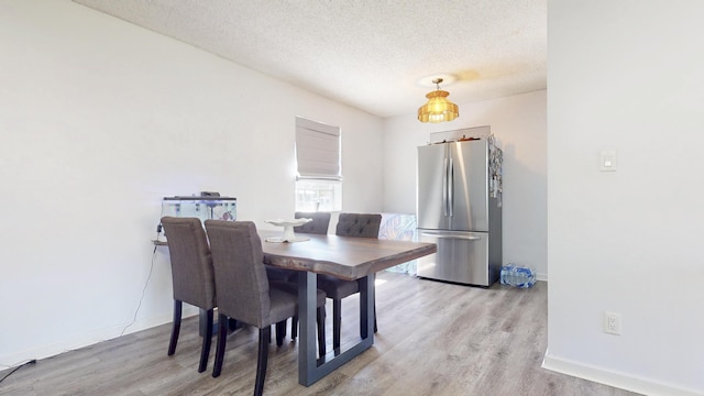 dining room with light wood-type flooring, baseboards, and a textured ceiling