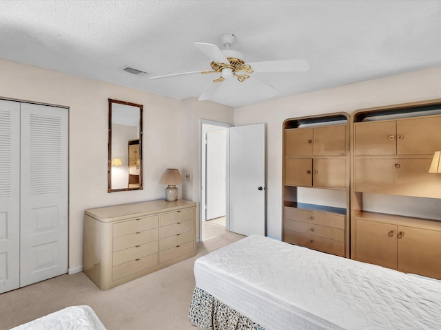 bedroom with visible vents, light colored carpet, a closet, a textured ceiling, and a ceiling fan