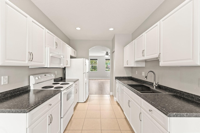 kitchen featuring a sink, white appliances, arched walkways, and dark countertops