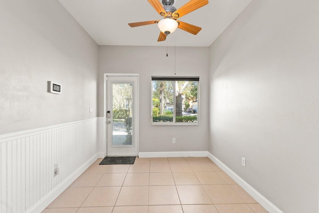 doorway with light tile patterned floors, baseboards, ceiling fan, and wainscoting