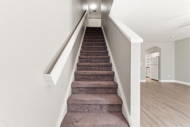 staircase with baseboards, arched walkways, and wood finished floors