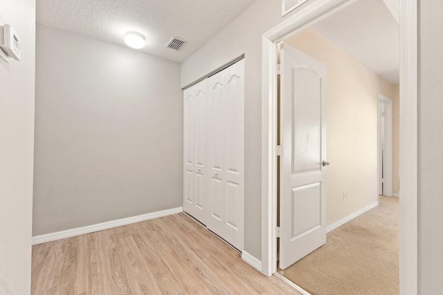 hallway with visible vents, light wood-style flooring, a textured ceiling, and baseboards