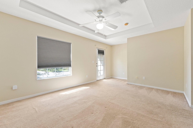 spare room featuring visible vents, baseboards, ceiling fan, a raised ceiling, and light colored carpet