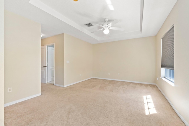 empty room featuring visible vents, light carpet, a raised ceiling, baseboards, and ceiling fan